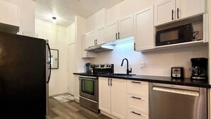 A modern kitchen with stainless steel appliances, white cabinetry, and a black countertop. - Cute little apartment in the city center (Québec)