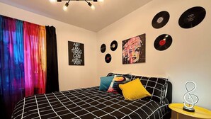 A bedroom with a black and white checkered bedspread, colorful curtains, a black and white patterned sofa, a small round table with a decorative item, and wall decorations including vinyl records and a poster. - Charming, well-furnished apartment (Québec)