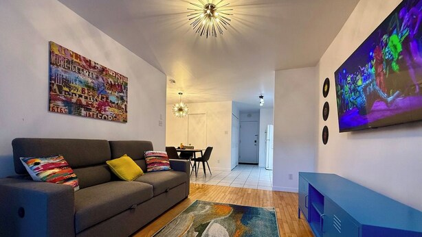 A modern living room with a sofa, a colorful rug, a television, and a ceiling light fixture. - Charming, well-furnished apartment (Québec)