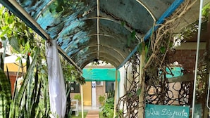 A covered walkway with potted plants and a sign in Spanish. - Hotel Junior (Caazapá)