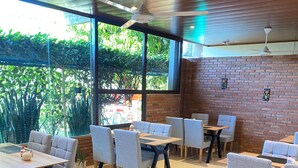 A restaurant with indoor seating, large windows, and a brick wall. - Hotel Junior (Caazapá)
