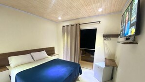 A hotel room with a bed, a desk, a chair, a TV, and a window with curtains.