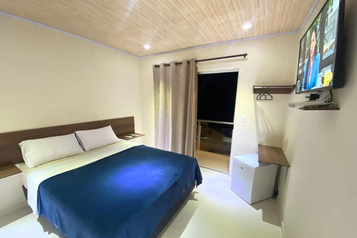A hotel room with a bed, a desk, a chair, a TV, and a window with curtains.