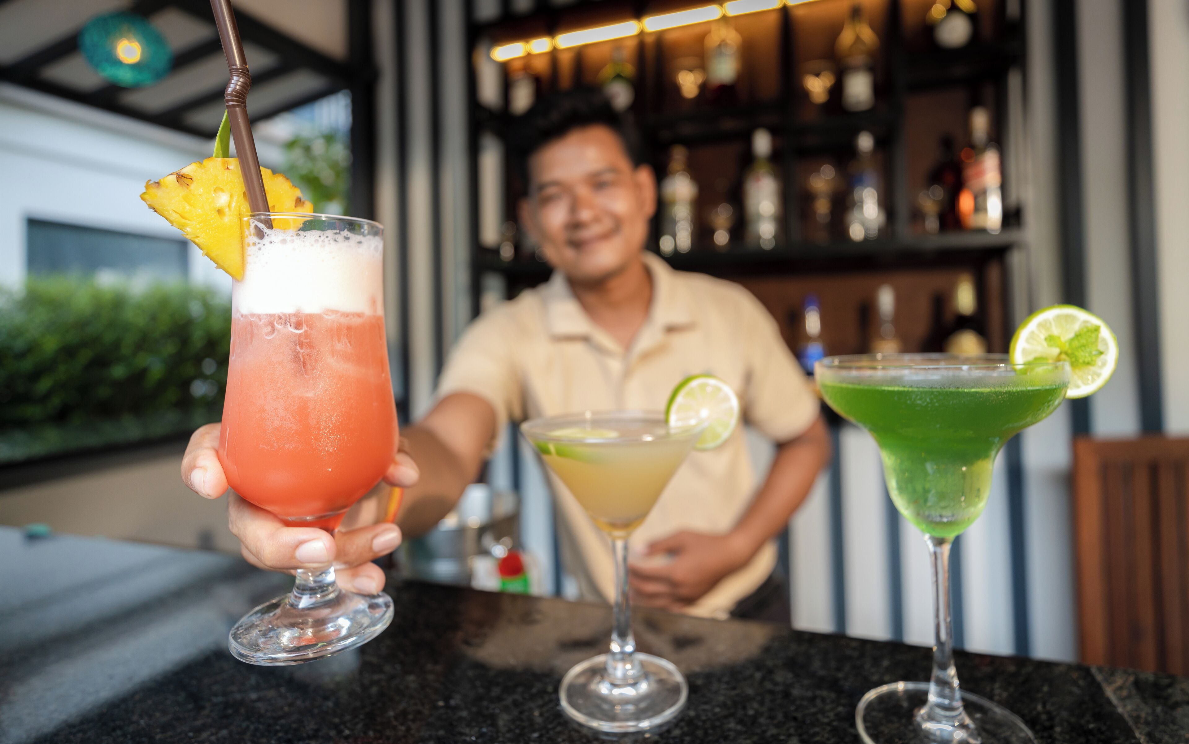 Un barman tient deux verres, l’un garni d’une tranche d’ananas et l’autre d’une tranche de citron vert.