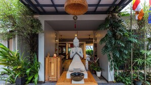 Ein friedlicher Eingangsbereich mit Buddha-Statue, einem Holztisch mit einer Schüssel und üppigem Grün.