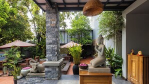 Ein Innenhof mit Steinsäulen, einer Buddha-Statue und Außenbestuhlung unter Sonnenschirmen.