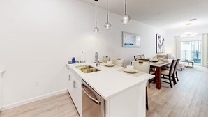 Een moderne keuken met een centraal eiland, een eetgedeelte met tafel en stoelen, en hangende verlichting.