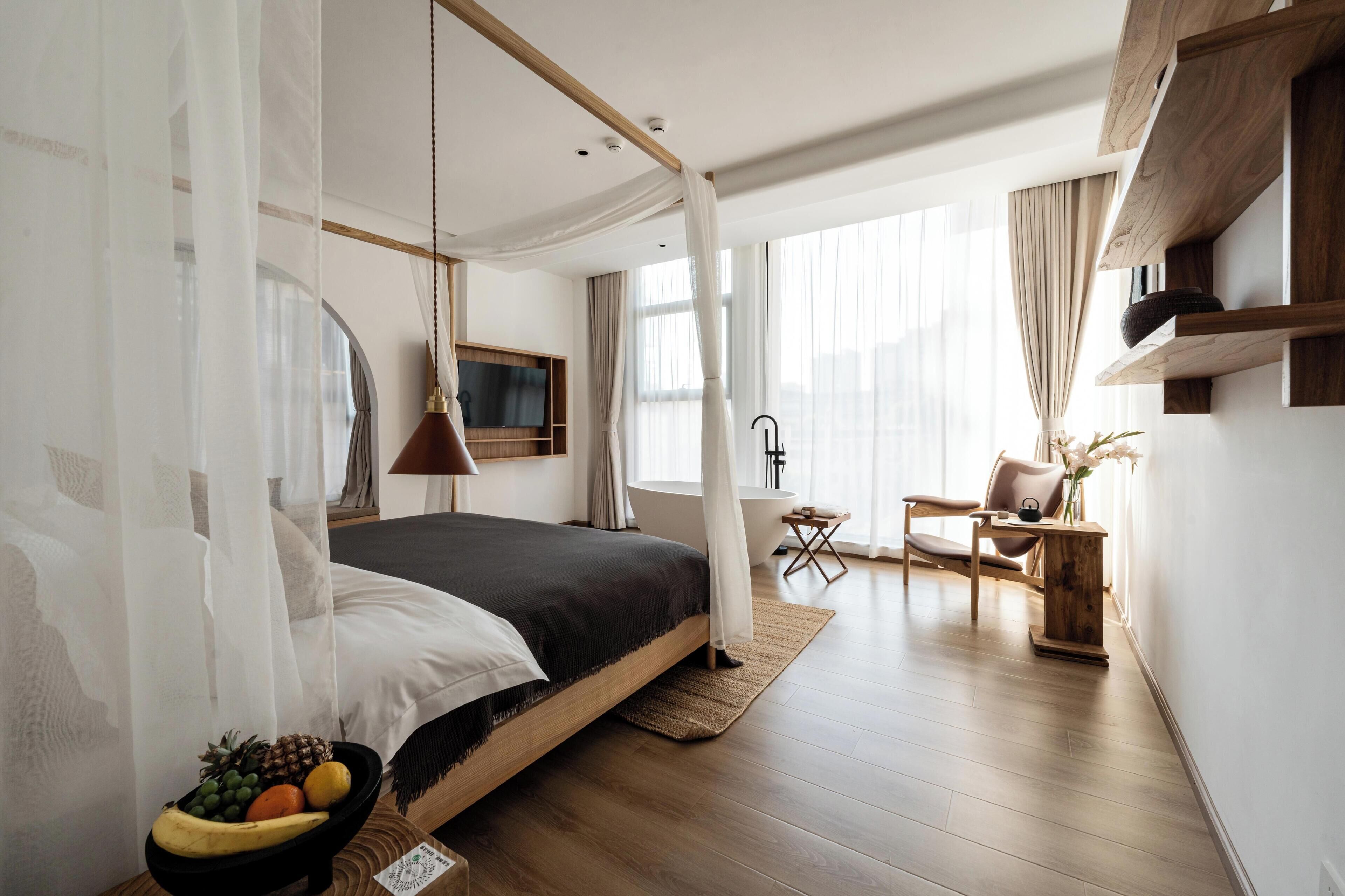 Un dormitorio moderno con una cama grande, una mesita de noche y un frutero. Hay una silla y una pequeña mesa con un jarrón de flores.