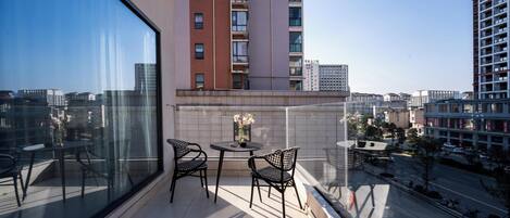 A balcony with a table and chairs, a vase with flowers, and a cityscape view.