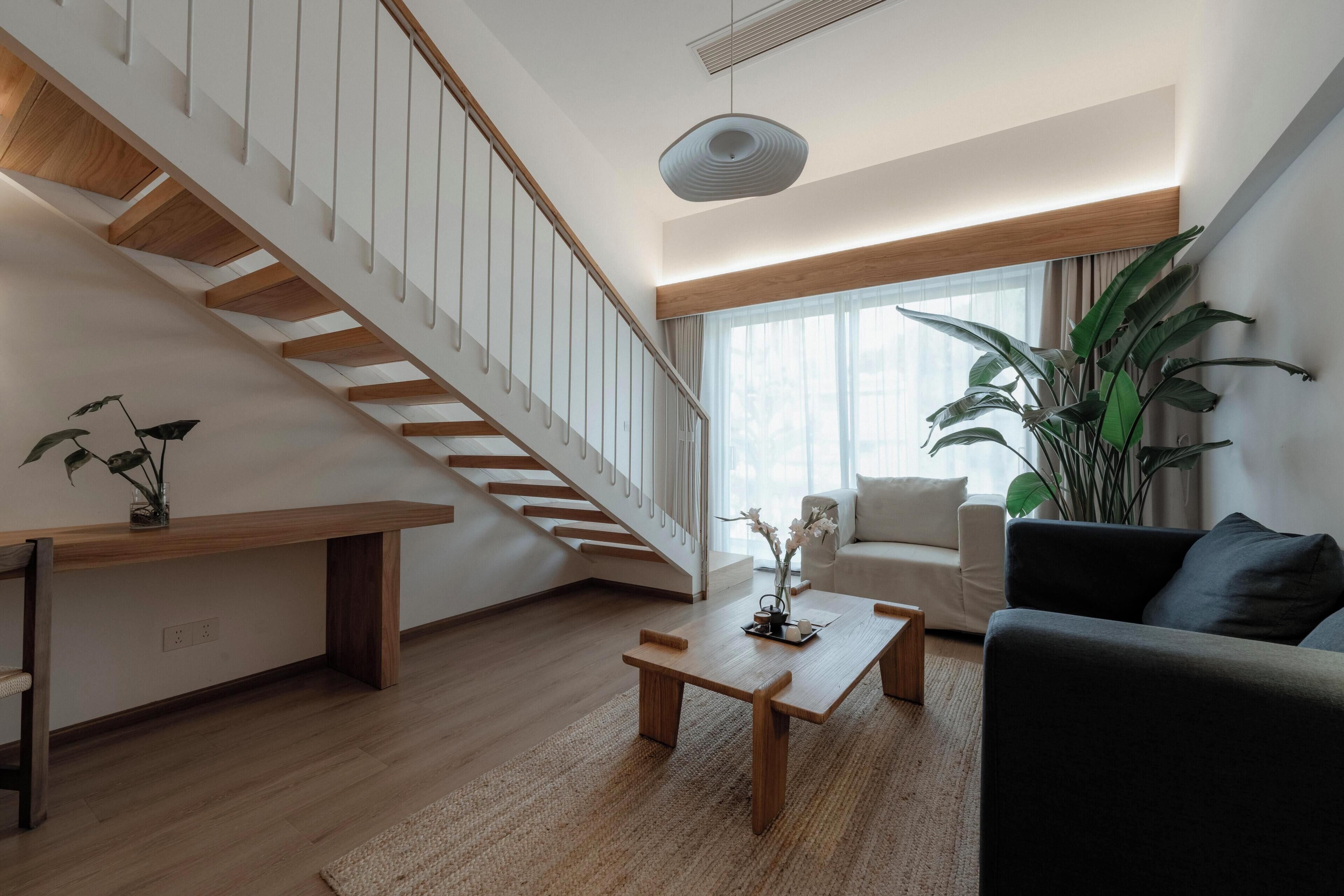 A modern living room with a wooden staircase, a sofa, a coffee table, and a large plant.