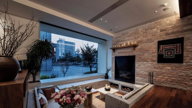 A modern living room with a stone fireplace, a large window overlooking a cityscape, and a cozy seating area. - Leli Villa Designer - Vacation Homestay (Qiandongnan)