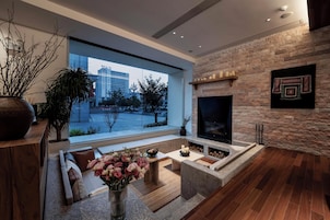 Una sala de estar moderna con chimenea de piedra, un ventanal con vistas a un paisaje urbano y un rincón de asientos acogedor.