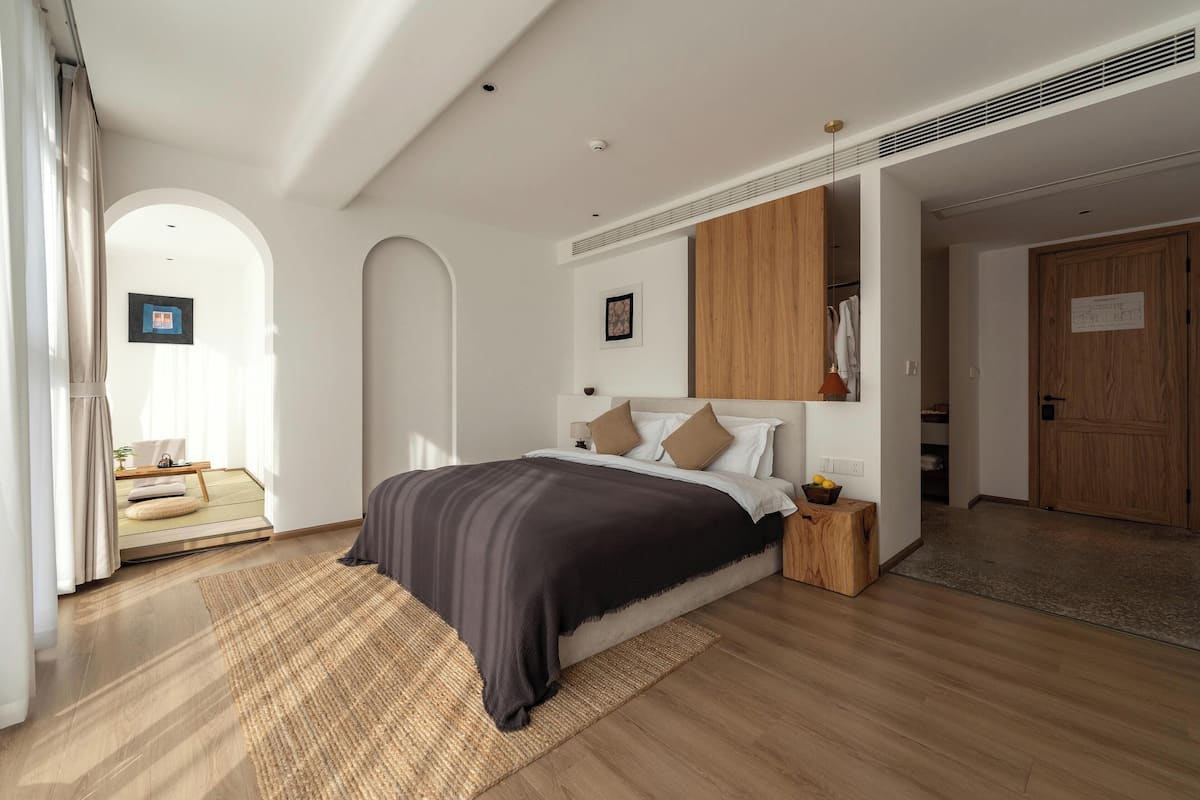 Een moderne slaapkamer met een groot bed, houten hoofdeinde en uitzicht op een gang.