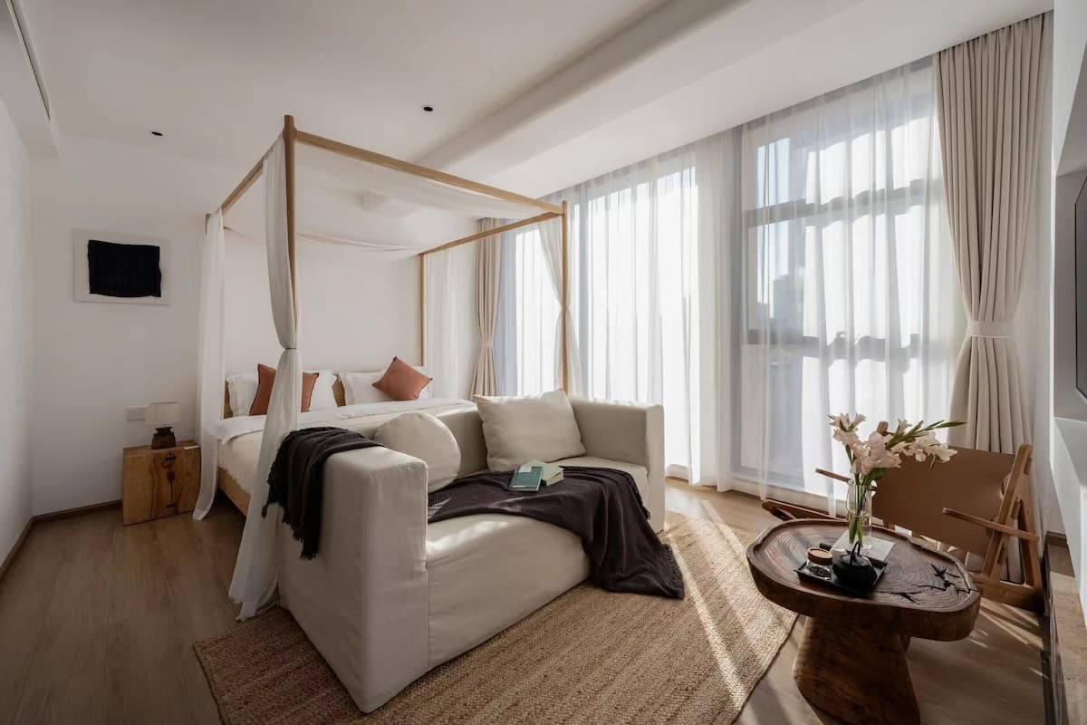 Een moderne slaapkamer met een hemelbed, een bank, een klein tafeltje met een vaas en een houten nachtkastje.