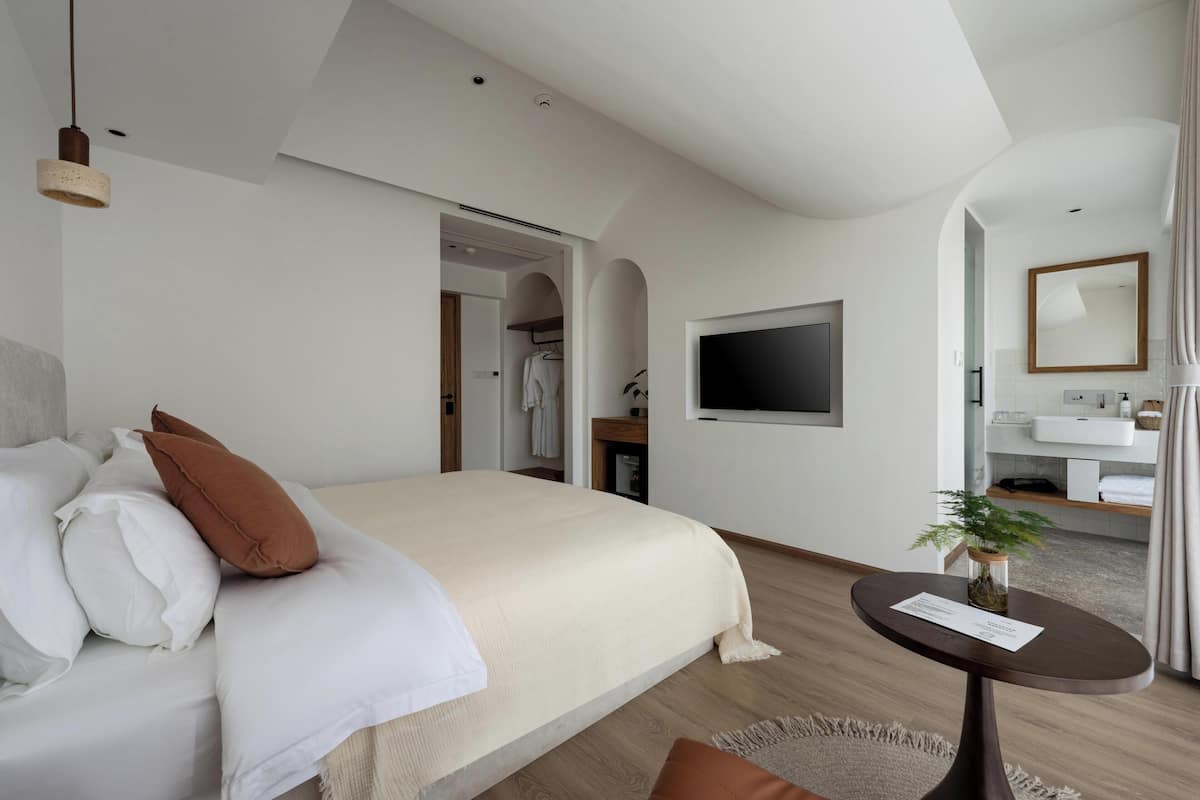 Een moderne hotelkamer met een groot bed, een televisie, een klein tafeltje met een plant en een badkamer zichtbaar door een open deur.