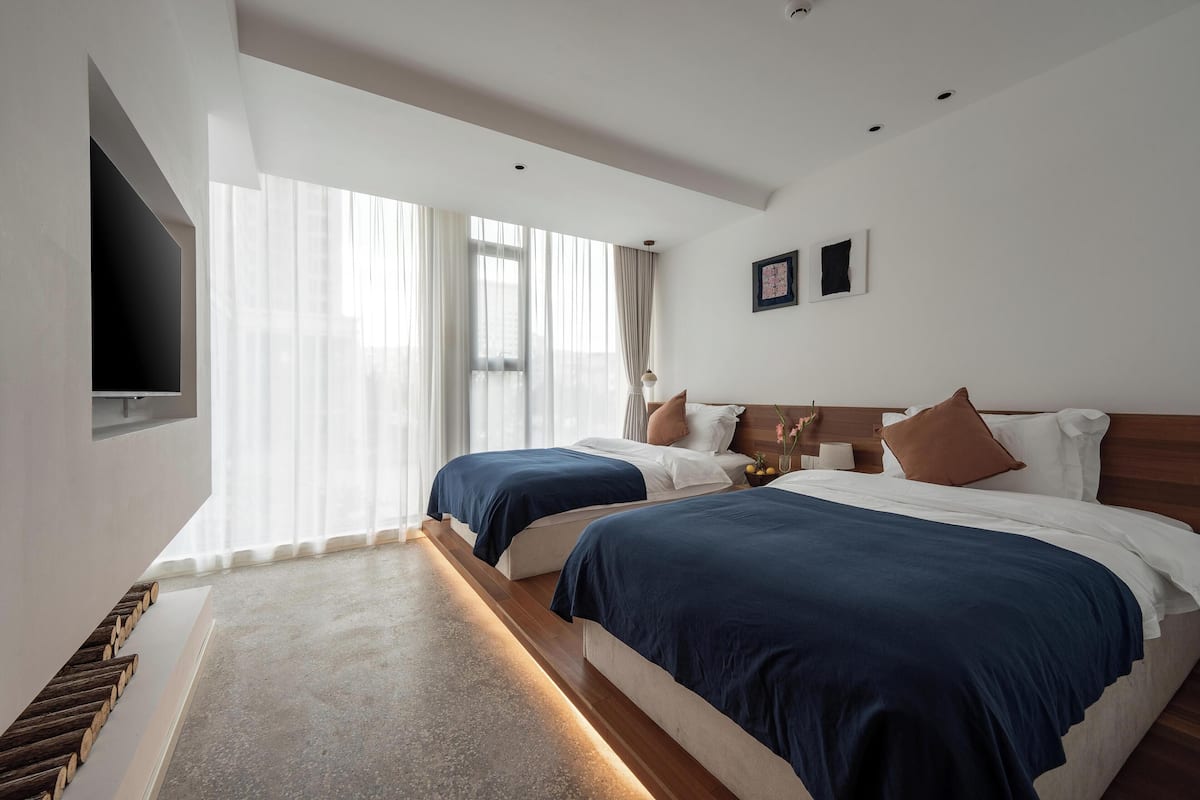 Een hotelkamer met twee bedden, een flatscreen televisie aan de muur en een groot raam met dunne gordijnen.