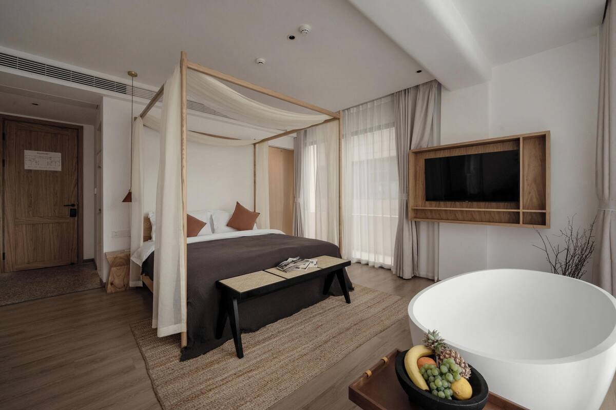 Een moderne slaapkamer met een hemelbed, een grote flatscreen televisie, een vrijstaand bad en een klein tafeltje met fruit.
