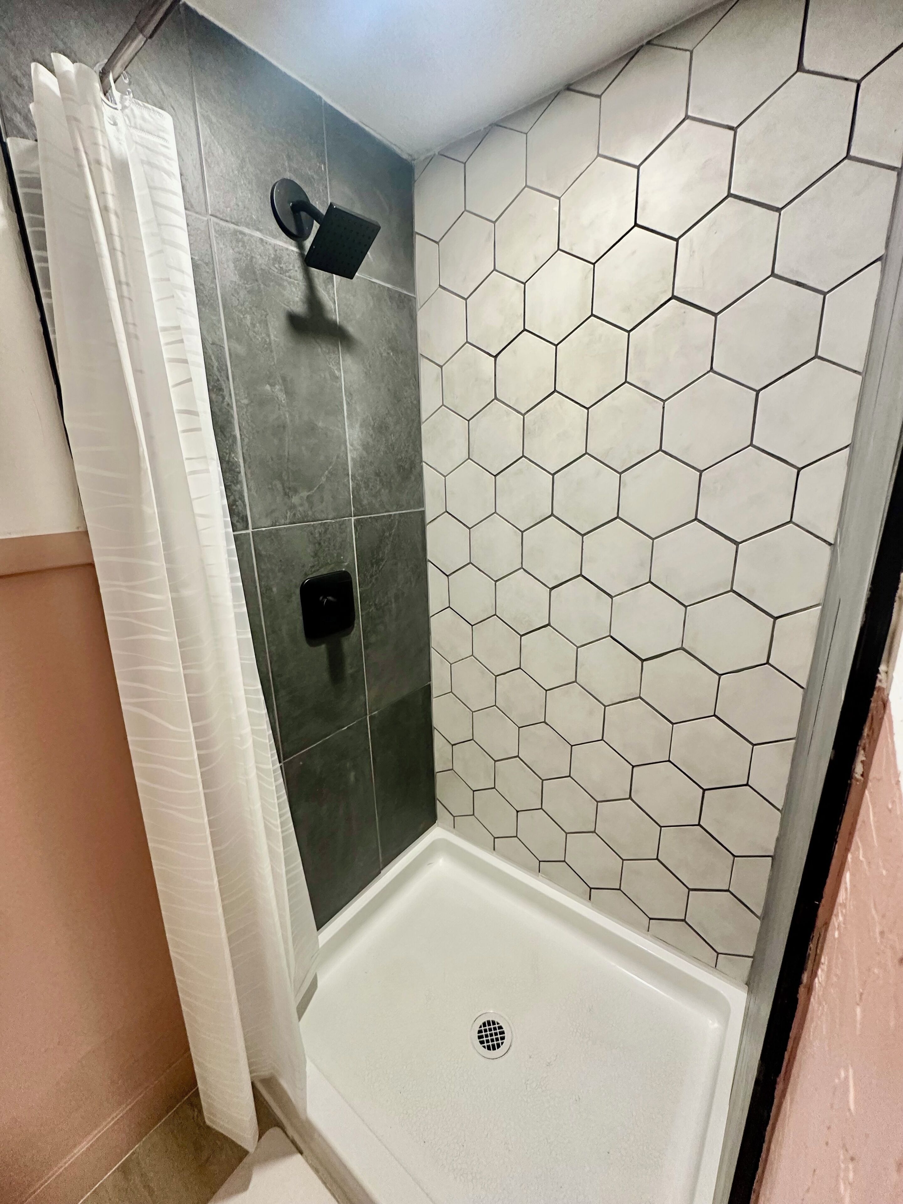 A shower with a hexagonal tile wall, a showerhead, and a drain.