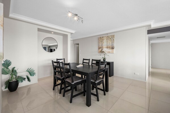 A dining area with a black table and chairs, a round mirror on the wall, and a painting above the table. - Crown Towers Resort - Luxury Apartment (Surfers Paradise)