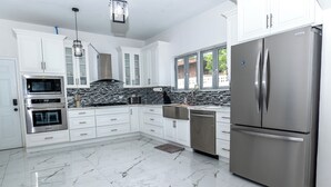 Een moderne keuken met witte kasten, een roestvrijstalen koelkast, een inbouwoven en een zwart-wit betegelde achterwand.