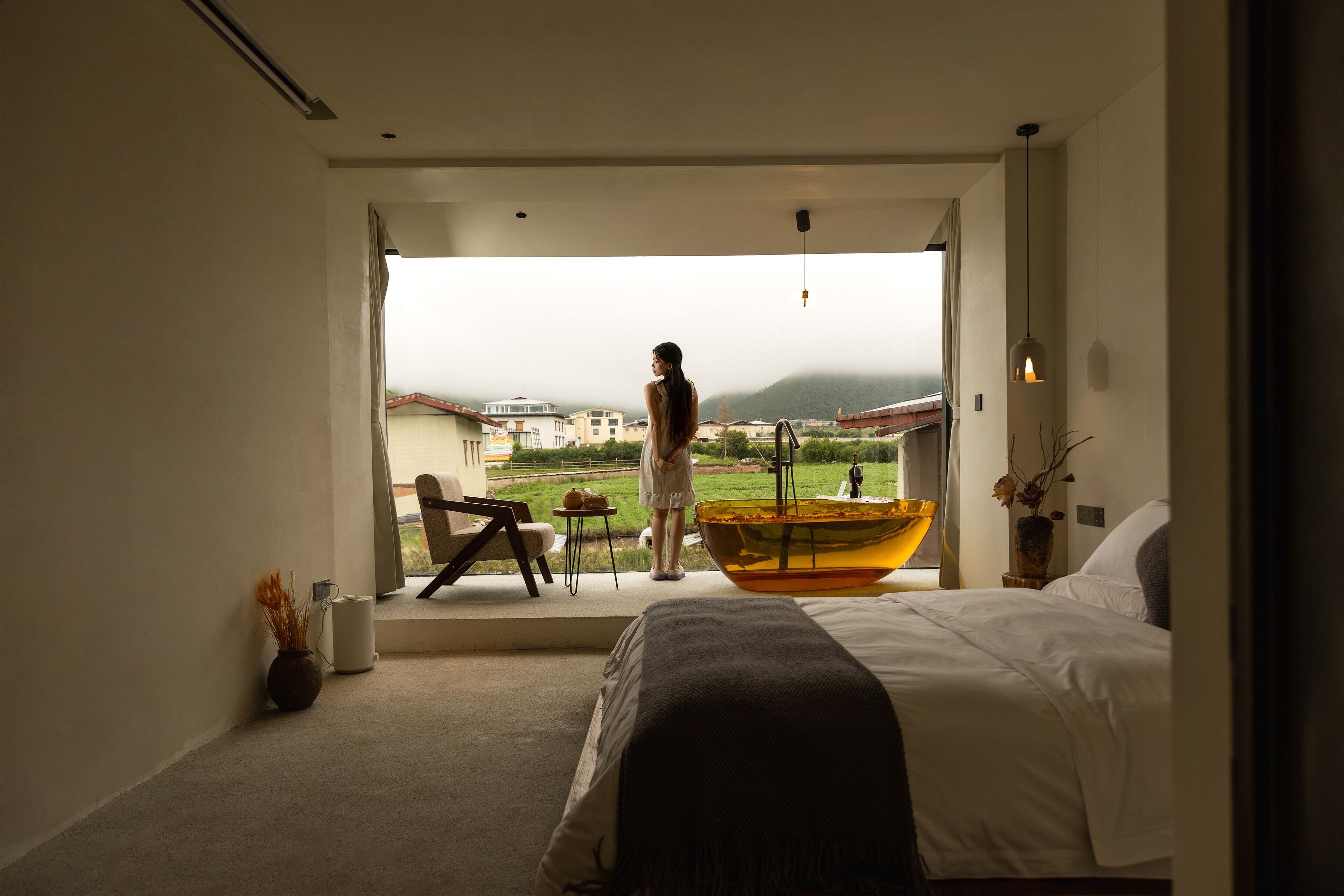 Ein Schlafzimmer mit einem großen Bett, Blick ins Freie, einem kleinen Tisch mit Stuhl und einer Vase mit getrockneten Blumen.