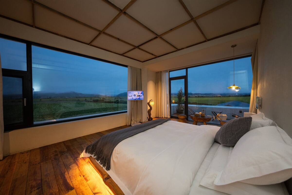 Quarto com cama grande, vista para o campo e design de teto moderno.