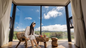 A person sitting on a wooden chair by a window with a view of a mountainous landscape. - LOST VILLA-ff (Deqin)
