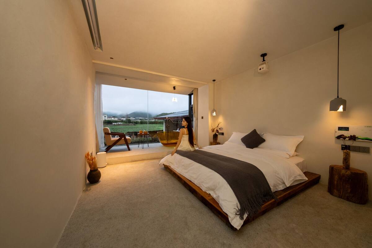 Quarto moderno com cama grande, vista para o exterior e uma pequena varanda.