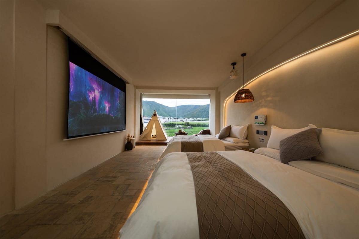Quarto de hotel moderno com uma cama grande, uma TV de tela plana, uma estrutura em forma de tenda e vista para montanhas através de uma grande janela.