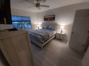 A bedroom with a bed, bedside tables, a ceiling fan, a window, and a door.