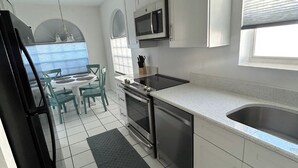 Una cocina moderna con armarios blancos, un refrigerador de acero inoxidable, un microondas y un fregadero.