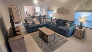 Una sala de estar moderna con un sofá azul, una mesa de centro de madera y un comedor con una cocina al fondo.