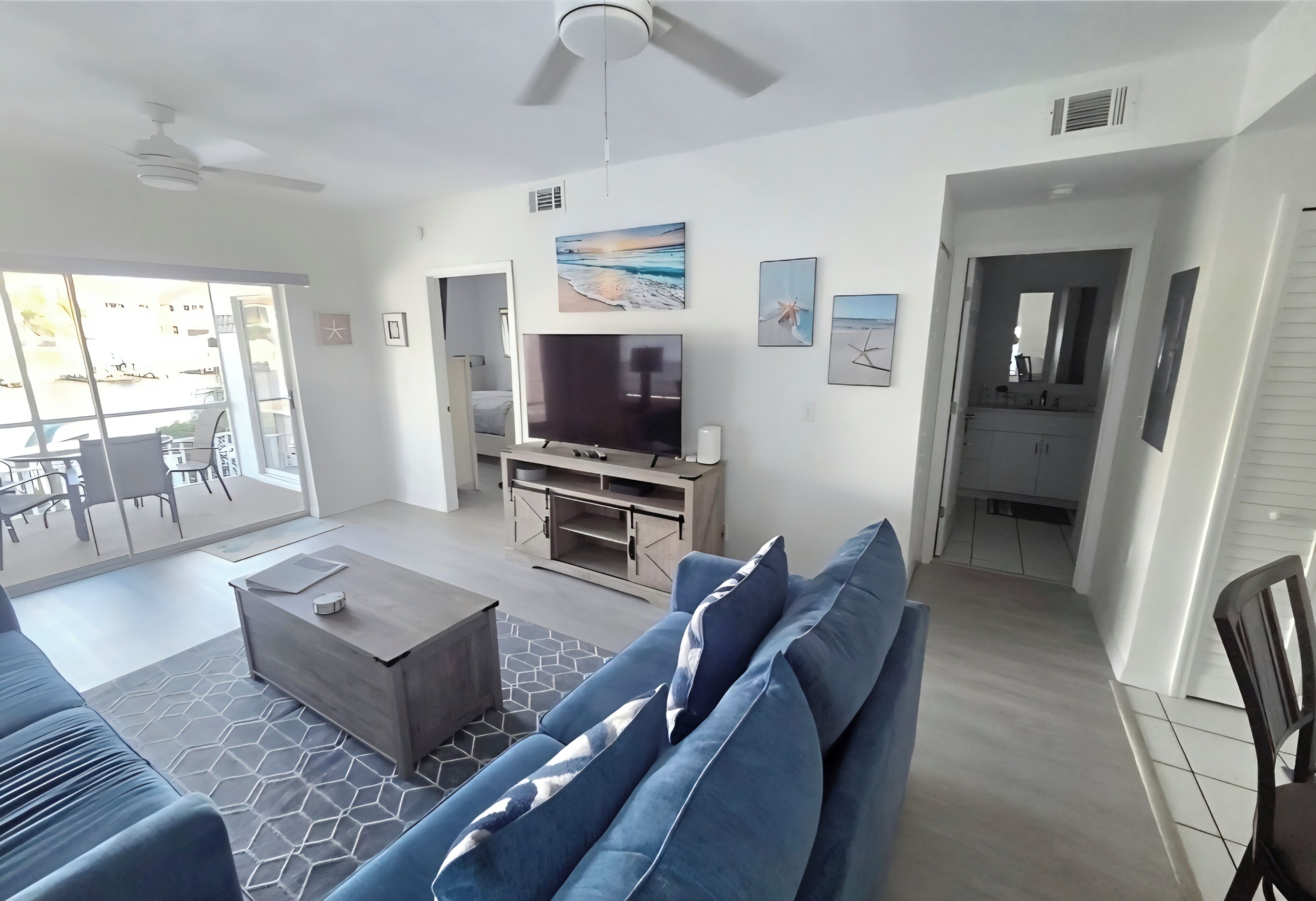 A modern living room with a flat-screen TV, a sofa, a coffee table, and a ceiling fan.
