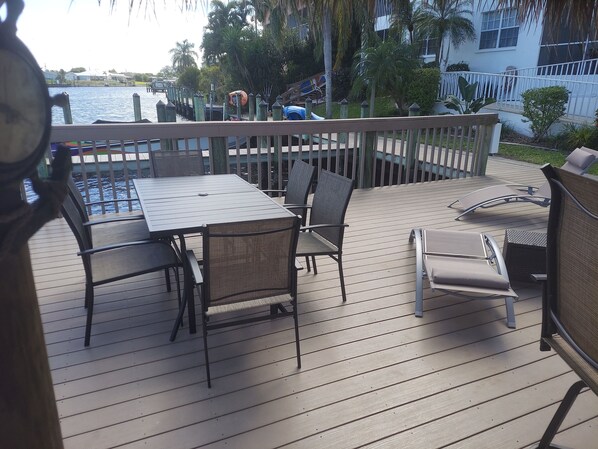 A wooden deck with a table and chairs, overlooking a body of water with a dock and boats.
