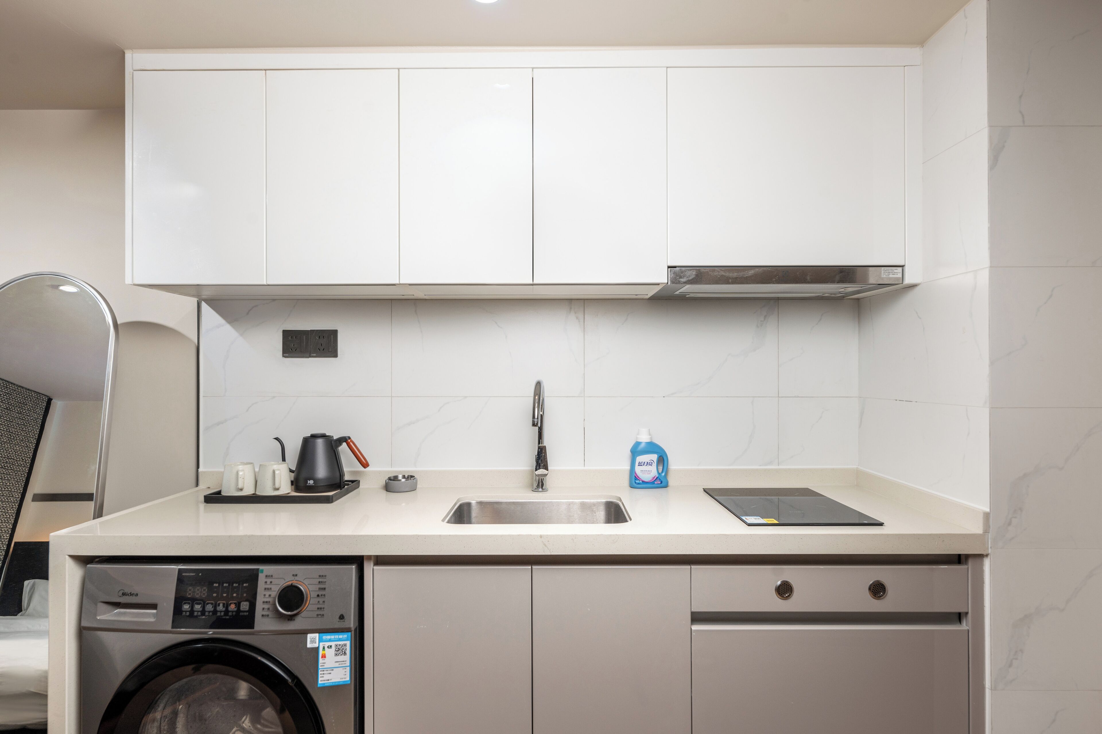 Una cocina compacta con lavadora, lavabo y encimera con hervidor, taza y jabón para platos.