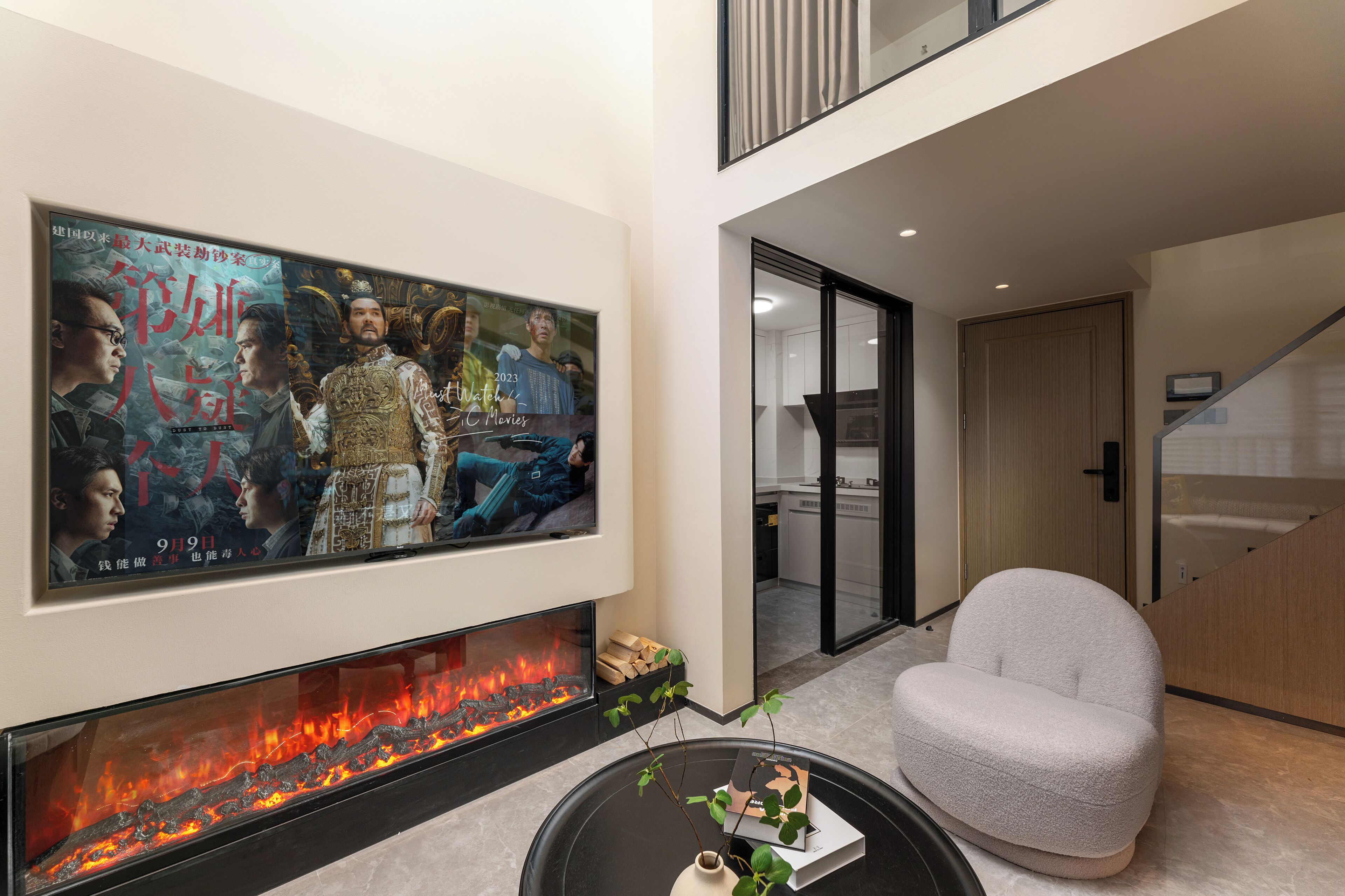 Una sala de estar moderna con un televisor de pantalla plana grande montado en la pared, una chimenea con fuego a la vista, un sofá gris confortable y una pequeña mesa con un florero y un libro.