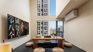 A modern interior with a wooden dining table, woven stools, a large framed artwork, and a view of high-rise buildings through large windows. - GTOOO Hotel (Guangzhou)