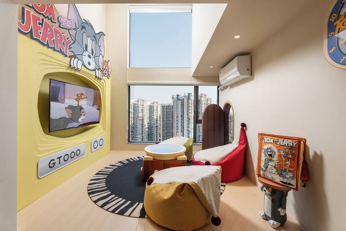 A modern living room with a large TV, comfortable seating, and a city view.