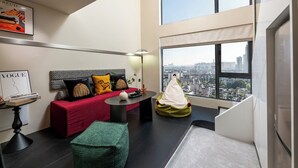 A modern living room with a red sofa, a green bean bag, a black coffee table, and a city view through large windows. - GTOOO Hotel (Guangzhou)