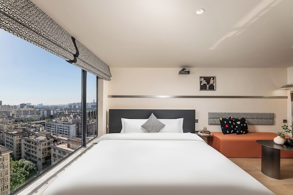 Un hotel moderno con una cama grande, vistas a la ciudad, una mesita pequeña y un sofá.
