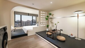 A modern hotel room with a large window, a washing machine, a small seating area, and a desk with a lamp. - GTOOO Hotel (Guangzhou)