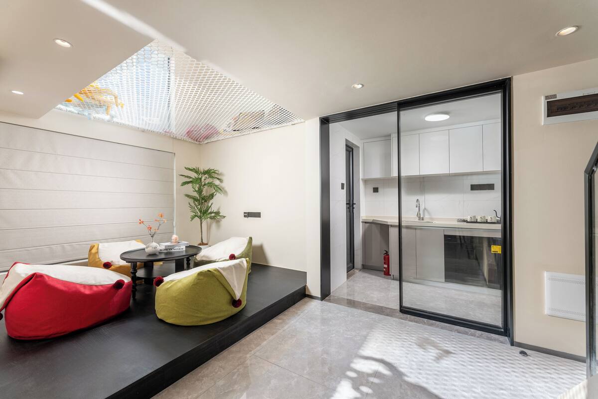 A modern living room with a sofa set, a small table with a vase, and a large window with a view of the kitchen.