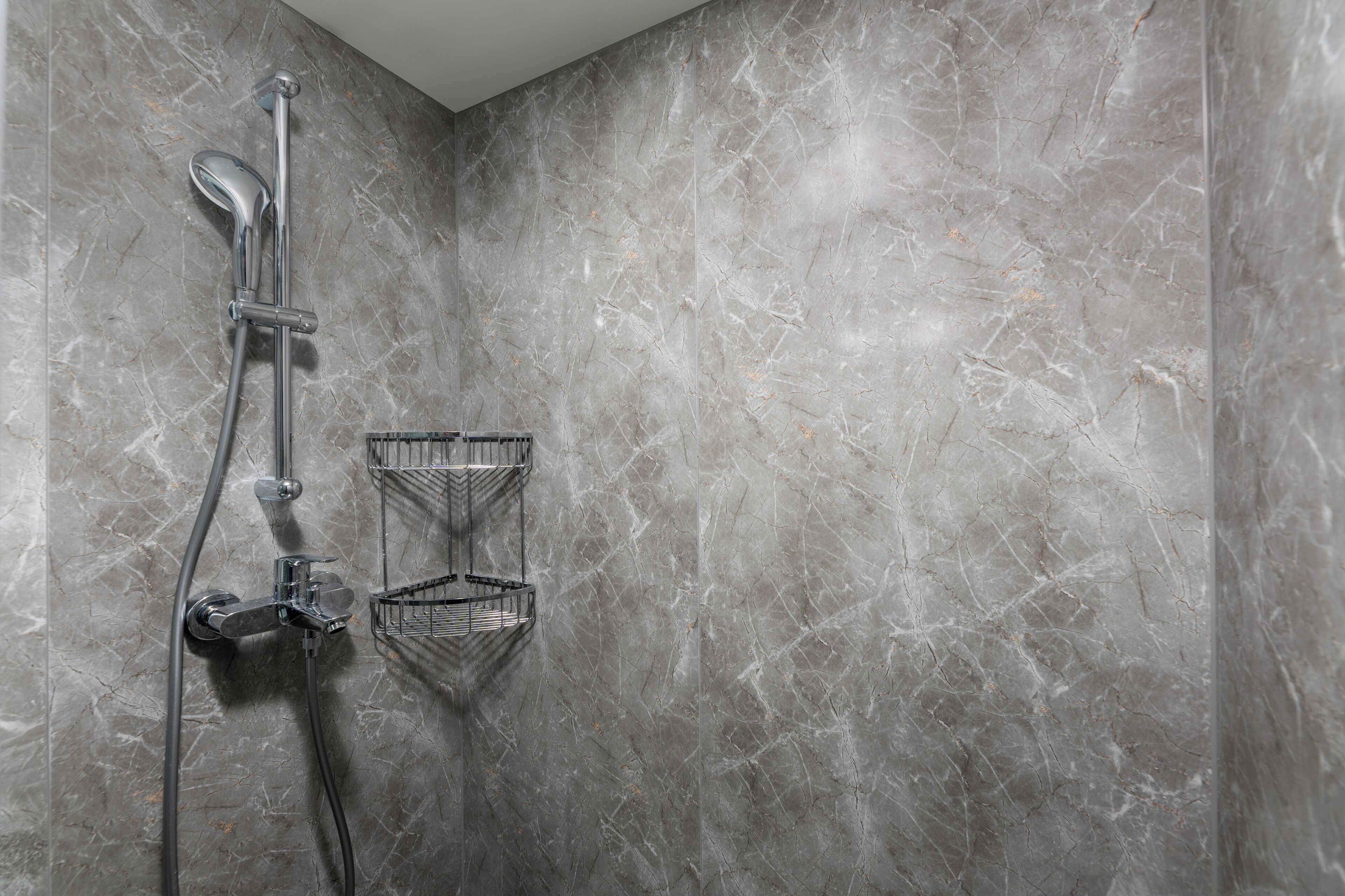 A shower with a chrome faucet and a metal shelf.