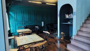 A spacious room with wooden tables and chairs, a staircase, and a bookshelf. - Youkoso Hostel Floripa (Florianópolis)