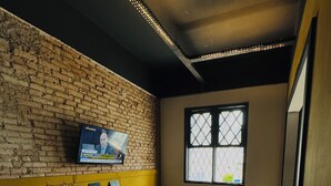 A cozy room with a brick wall, a television mounted on it, a window with a view, and two bean bags. - Youkoso Hostel Floripa (Florianópolis)