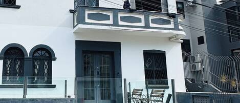 Una casa moderna de dos pisos con balcón, entrada protegida por un portón y antena parabólica visible.