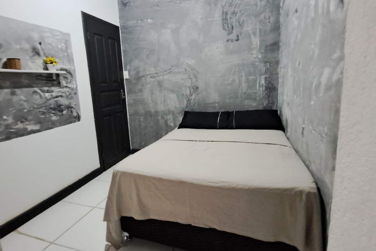 Une petite pièce étroite, avec un lit, une porte et un mur orné d’une fresque à motifs.