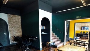A spacious room with a wooden floor, a dining area with a table and chairs, a staircase, and a seating area with a TV. - Youkoso Hostel Floripa (Florianópolis)
