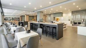 En moderne restaurant med flere spiseområder, en central bar og et køkken i baggrunden.