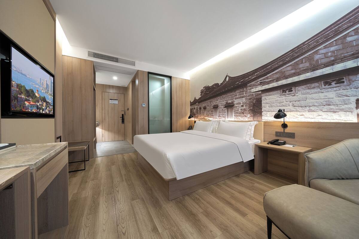 A modern hotel room with a large bed, a desk, a chair, and a TV.